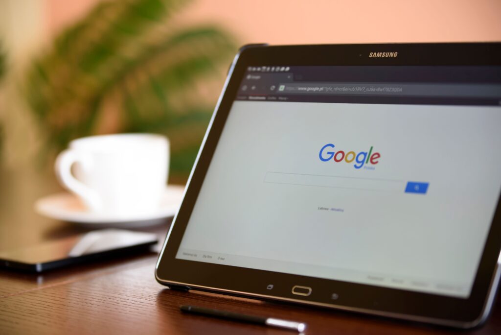 laptop z otwartą stroną Google na ekranie, w tle biała filiżanka i smartfon